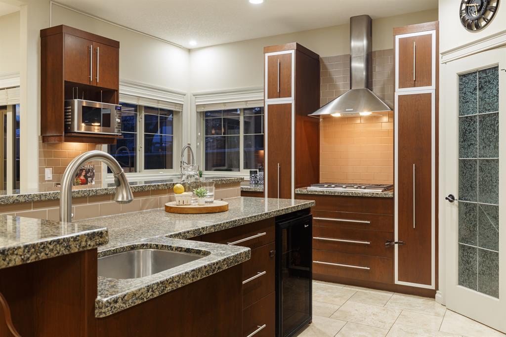 Gas cooktop under a stainless hood, island sink and beverage fridge